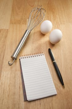 Mixer, Eggs, Pen and Pad of Paper on a wood background.