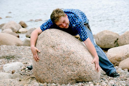 The young man tries to shift the big stone