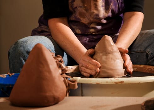 Closeup on hands of potter shaping clay wedge on wheel