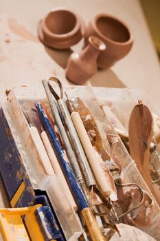 Tools for shaping clay with finished pots in the background