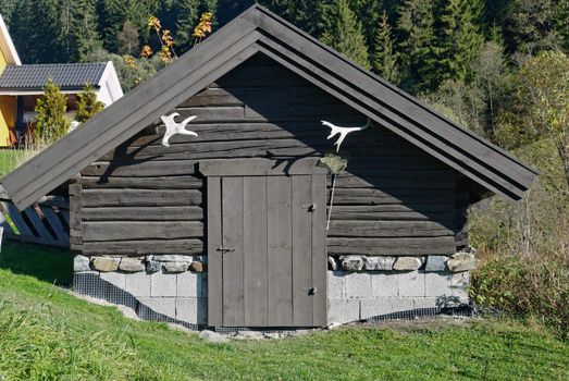 A small traditional Norwegian storage house or cellar, made of tared timber with moose horns.
