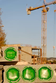 Concreted block at a construction site, plugged with green, with crane at the background
