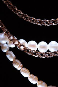 Closeup of pearl necklace and gold chain on dark background