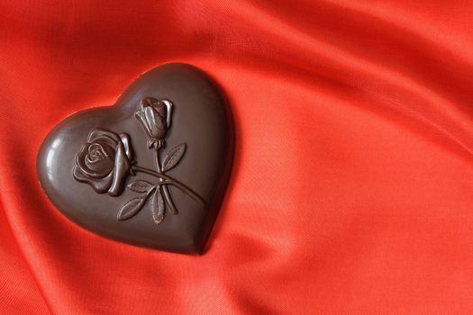 Closeup of chocolate heart lying on red silk textile with copy space