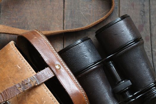 Closeup of old binoculars and leather case on wooden background