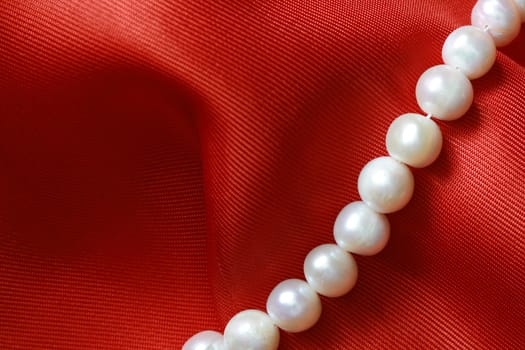Closeup of pearl necklace lying on red textile background