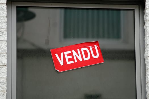 Window with Red and white sticker with word Vendu that means Sold in french