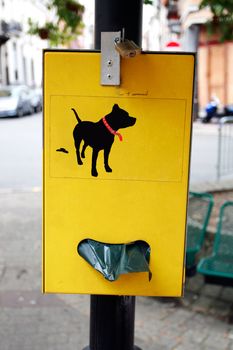 Yellow plastic bag dispenser for dog poo in park