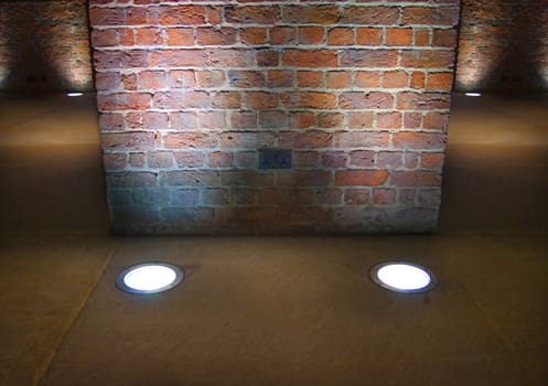 Very old (1854) interior brick wall lit up by spotlights set in a stone floor
