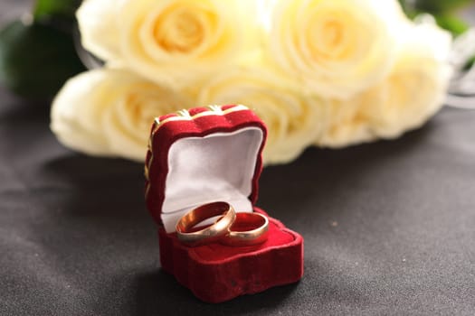 wedding rings, box and white roses on black background