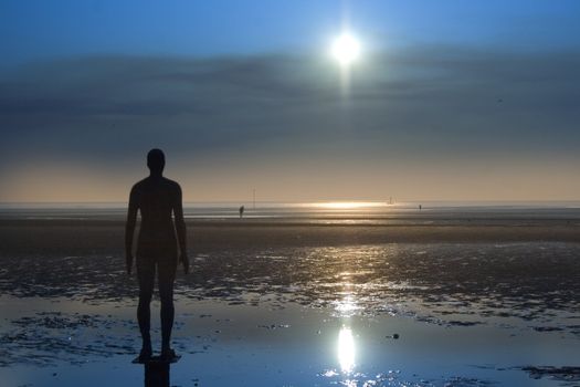 Iron statue on the beach silhouette against a clear blue sky
