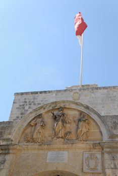 The entrance gate to Mdina on Malta, with Maltese flag St. Peter sculpture group. The writing is in Latin from the 14th century.
