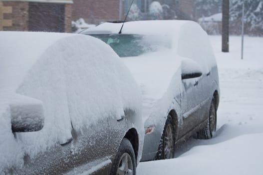 Two cars covered by snow during winter storm.