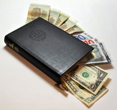 Black leather bible with money (Dollars, Euro, Rubles) poking out on white background