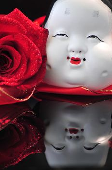 Asian beauty mask and red rose beauty, both reflected on a dark mirror surface