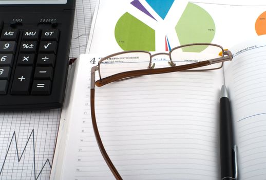 Glasses and pen on an open diary, chart and a calculator.