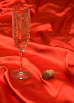 A glass of champagne and the cork on a red cloth.