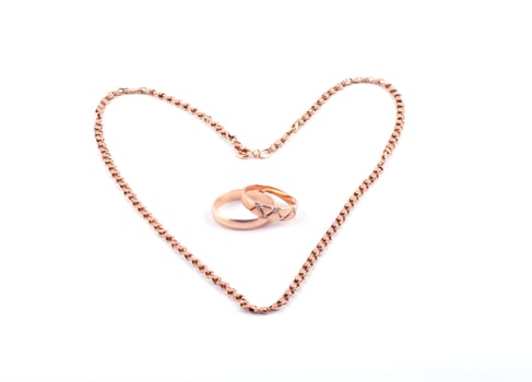 Heart from a gold chain and two wedding rings on a white background.