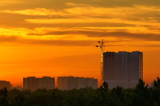 construction of a building, cranes and other machinery as silhouettes against a background of red sunset sky