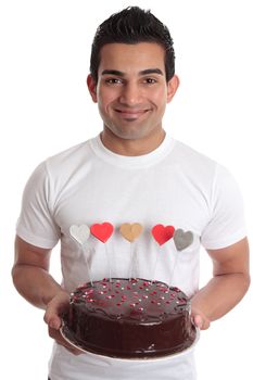 Amorous man carries a delicious baked chocolate coated cake decorated with love hearts in red gold pink and silver and white.