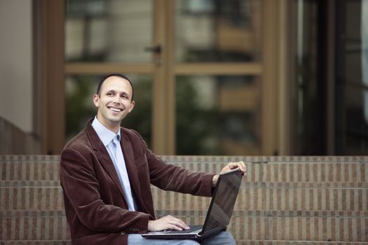 Young happy business man working outdoors with the laptop and looking high up