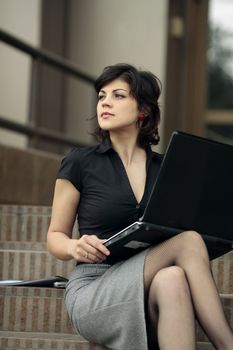 young attractive lady with a laptop on the stairs in front of an office building looking up