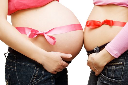 Closeup on two pregnant women measuring their belly, second and third trimester