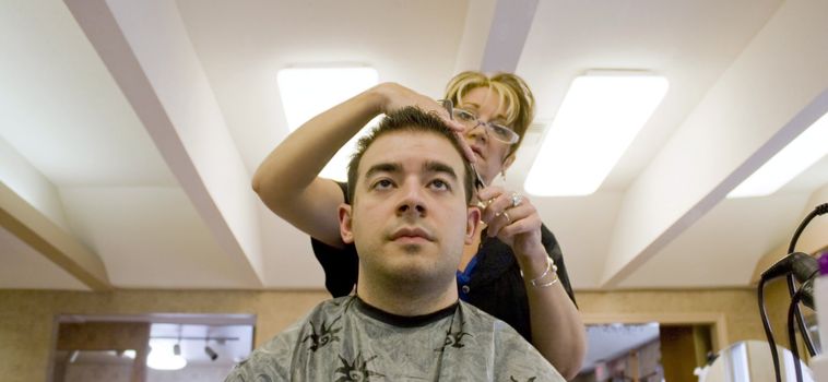 A young man is getting his hair cut by a hairdresser at the salon