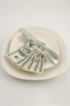 Five 100 US Dolllar bills on a white plate with a knife and fork