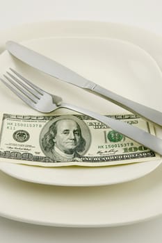 A one hundered United States dollar on a plate with a knife and fork