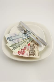 Canadian bills on a plate with a stainless steel knife and fork with a white background
