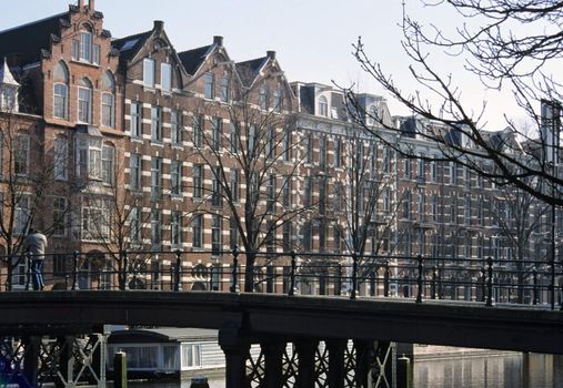 A lone man walks over a bridge toward a row of traditional canal houses in Amsterdam, the Netherlands