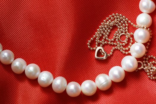 Pearl necklace and gold chain lying on red silk background