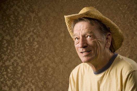 Senior man in a straw hat in front of gold wallpaper