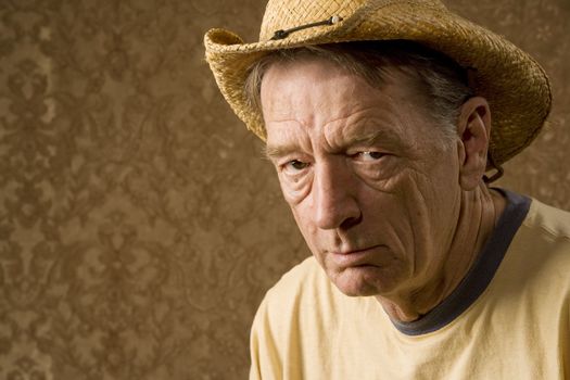 Senior man in a straw hat in front of gold wallpaper