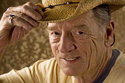 Senior man tipping a straw hat in front of gold wallpaper