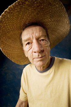 Senior man in a  big straw hat in front of blue set wall