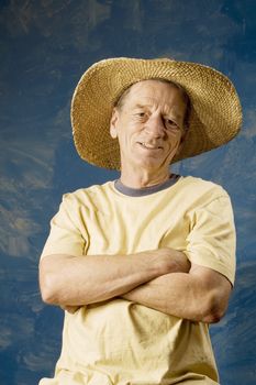 Senior man in a straw hat in front of blue set wall