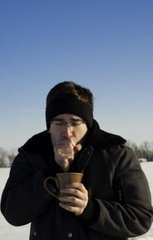 A man outside in the winter is warming his hands and holding a cup of coffee