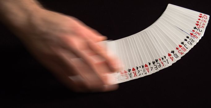 Hand spreading playing cards against black background.