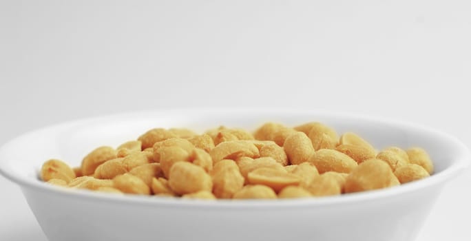 White bowl of peanuts against a white background.