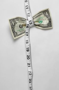 Dollar bill being squeezed by tape measure on white background.