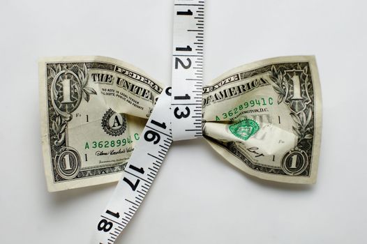 Dollar bill being squeezed by tape measure on white background.