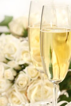 Close-up of champagne glasses with a bouquet of roses in background
