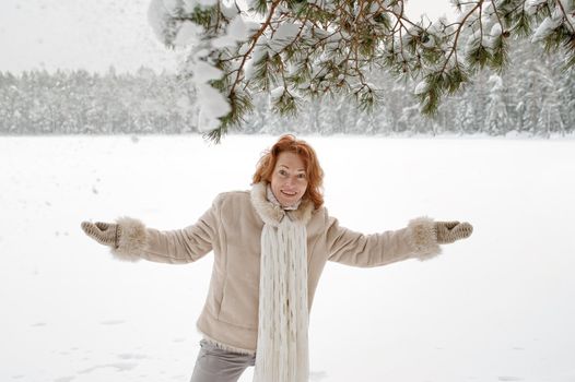 Attractive red-haired woman having fun on winters day in forest.