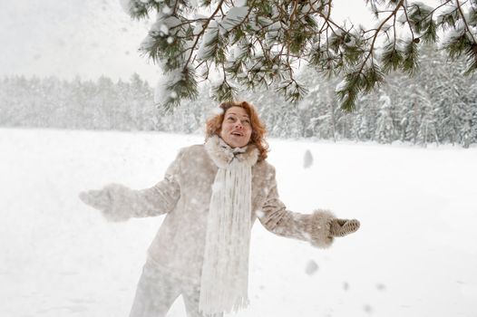 Attractive red-haired woman having fun on winters day in forest.