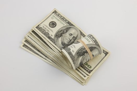 A roll and a stack of United States hundred dollar bills with a white background