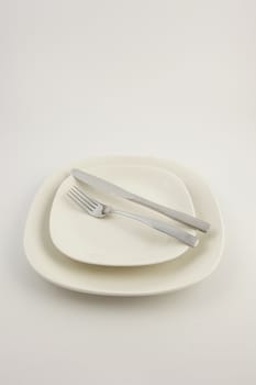 Two white plates and a stainless steel knife and fork on a white background