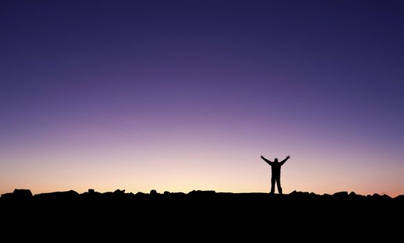 Silhouette of a man raising his hands into the sunrise after conquering a summit