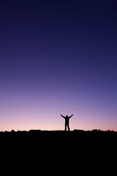 Silhouette of a man raising his hands into the sunrise after conquering a summit